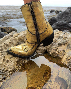 Mid-calf western-style boot featuring a distressed metallic finish, pointed toe, angled block heel, and contrast stitching. Designed with decorative panel overlays and a side zipper closure.
