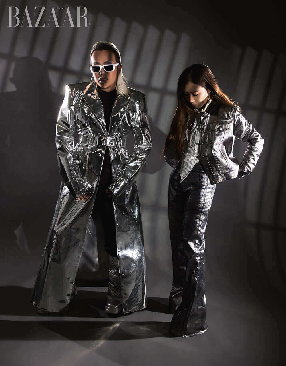 Two models in stylish metallic outfits posing confidently for a fashion photoshoot, with dramatic shadows.