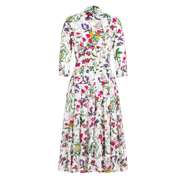 A white midi dress with an all-over print of colorful wildflowers in shades of pink, purple, yellow, and green. The dress has a shirt collar, 3/4 sleeves, a button-front, a pleated A-line skirt, and a matching fabric belt.