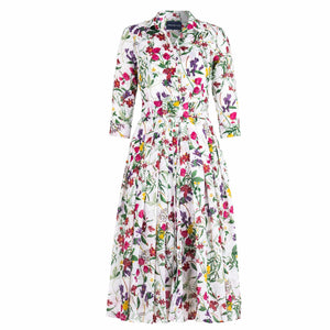 A white midi dress with an all-over print of colorful wildflowers in shades of pink, purple, yellow, and green. The dress has a shirt collar, 3/4 sleeves, a button-front, a pleated A-line skirt, and a matching fabric belt.