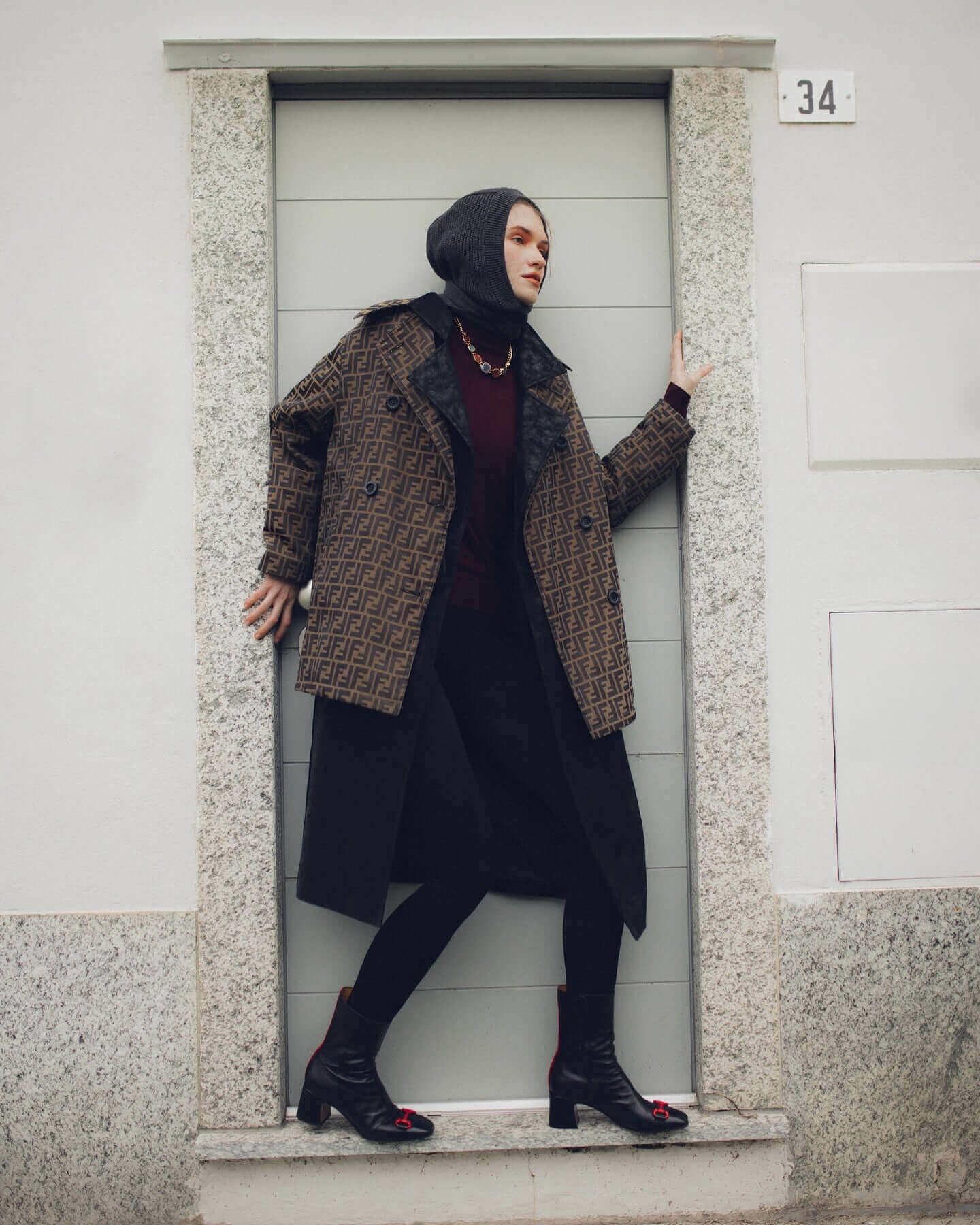 Fashionable model poses in a stylish patterned coat and headscarf against a modern door.