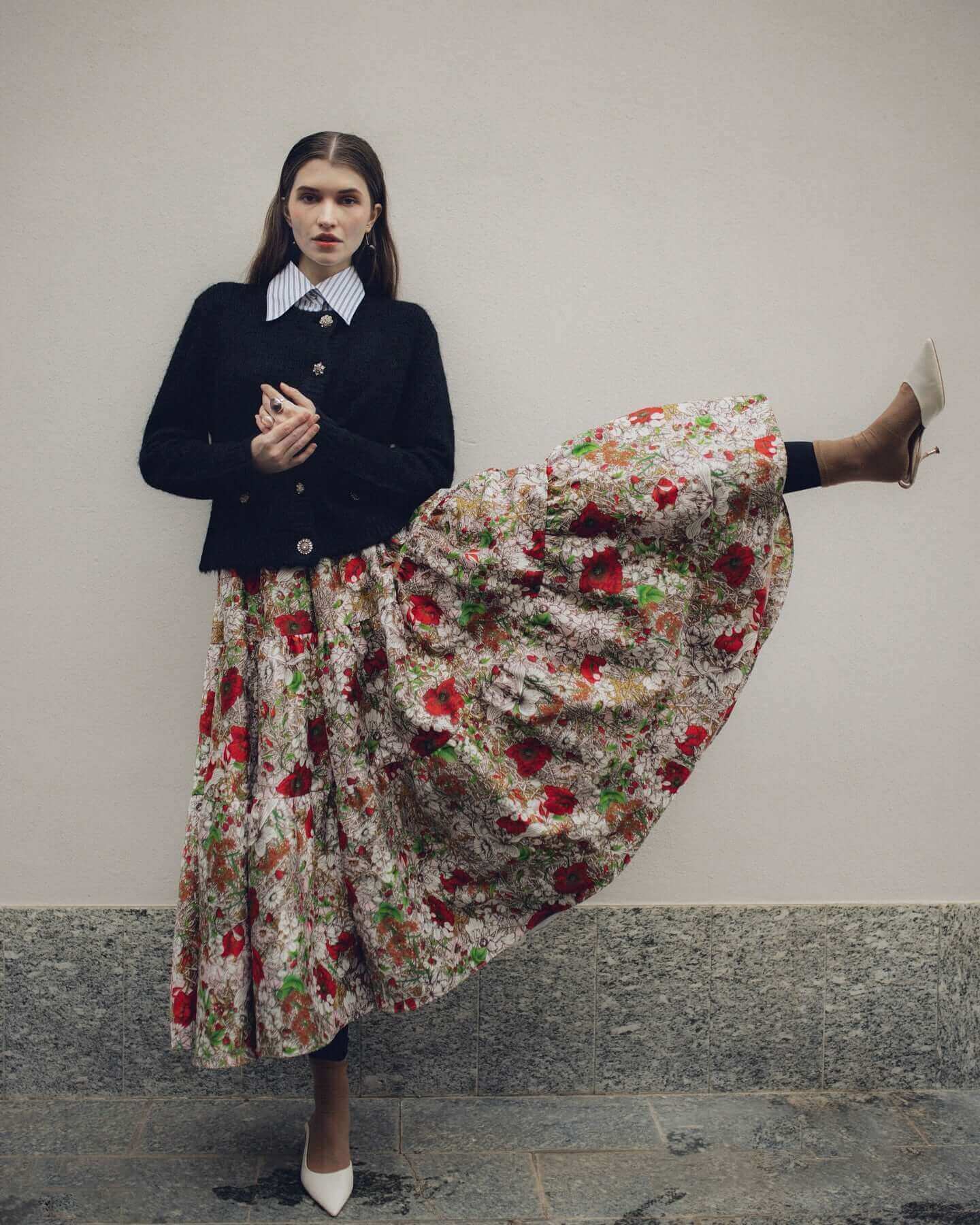 Fashion model in floral skirt and black cardigan, posing elegantly with a stylish stance.
