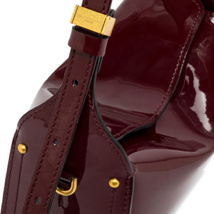 Close-up of a burgundy patent leather handbag with gold hardware on a white background