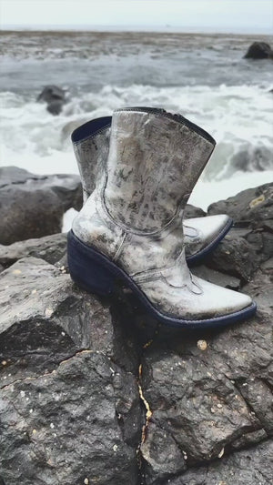 Mid-calf western-style boot featuring a distressed metallic finish, pointed toe, angled block heel, and contrast stitching. Designed with decorative panel overlays and a side zipper closure.