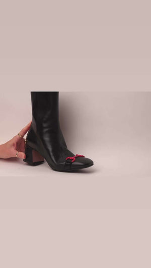A tall leather boot with a block heel and rounded toe, featuring a metal horsebit-style detail at the front and a small metal padlock accent near the top of the shaft. Designed by Madison in Beverly Hills and handcrafted in Italy