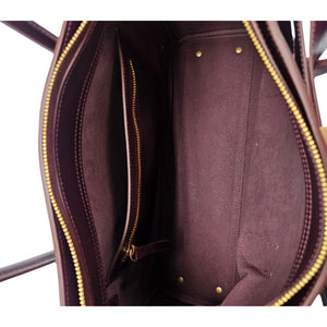A sleek, burgundy polished leather handbag with two slender top handles and a horizontal gold bar accent on the front.