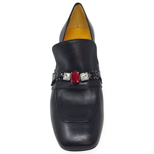 Black loafer shoe with a decorative buckle featuring a red gemstone and silver accents on a white background.