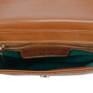Brown leather handbag with visible stitching and a brand label on a white background