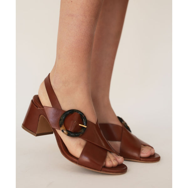 Brown open-toe sandals with a circular buckle on a neutral background