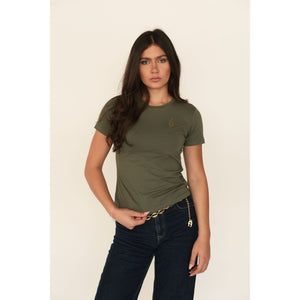 Woman wearing an olive green t-shirt and dark jeans on a beige background