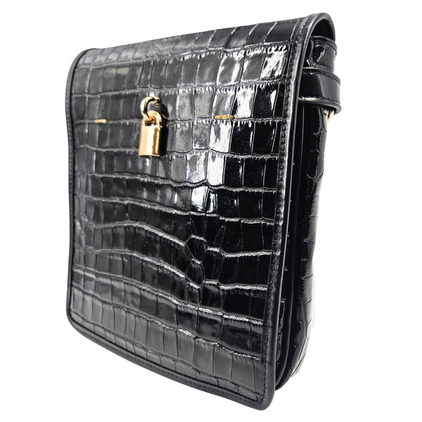 Black crocodile-patterned handbag with a gold clasp on a white background