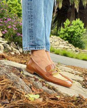 A leather loafer with a flat sole and rounded toe, featuring a contrasting vamp panel and dual chain accents across the upper. Designed by Madison in Beverly Hills and handcrafted in Italy.