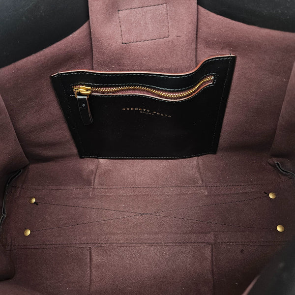 A sleek, black polished leather handbag with a wide opening, two top handles, and a horizontal gold bar accent on the front.