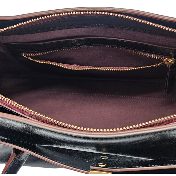 A sleek, black leather handbag with two slender top handles and a horizontal gold bar accent on the front.