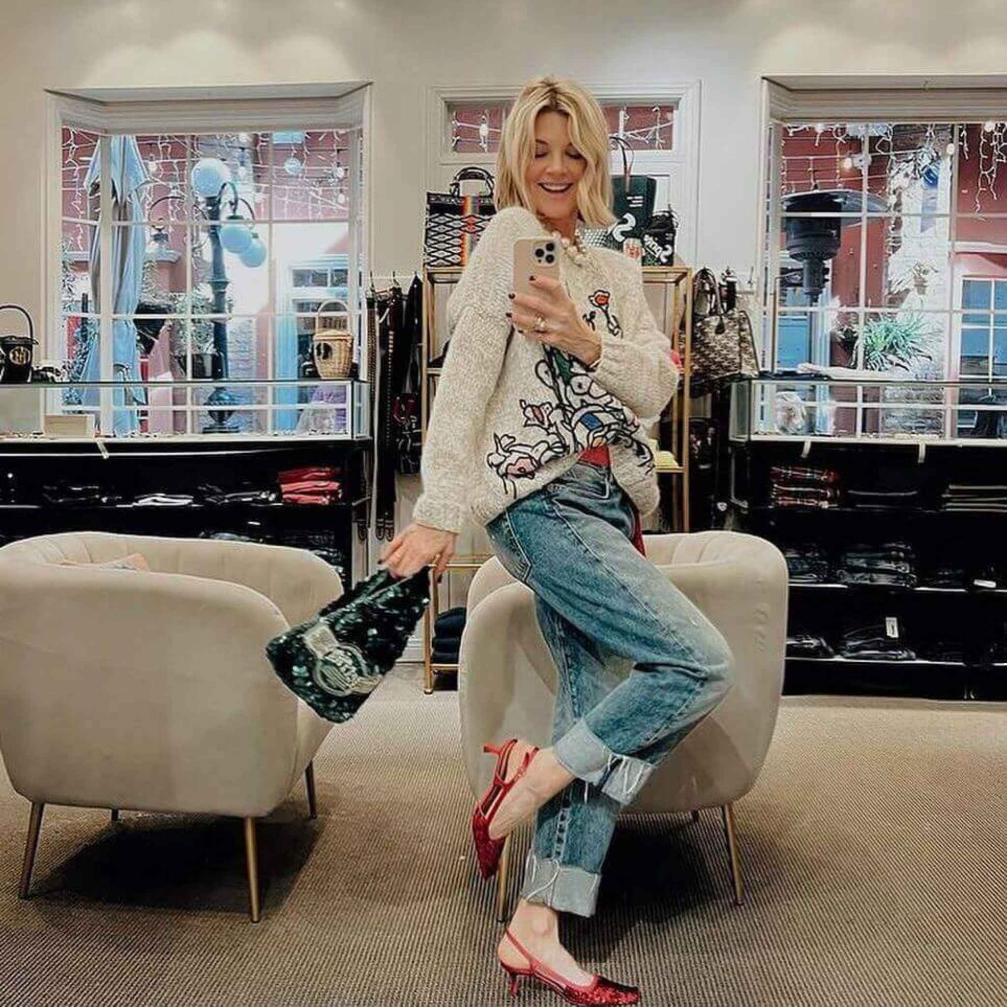 Woman in a store taking a mirror selfie wearing a patterned sweater and jeans.