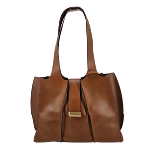 A mid-brown polished leather handbag with a wide opening, two top handles, a horizontal gold bar accent on the front, and a matching small brown pouch resting in front of it.