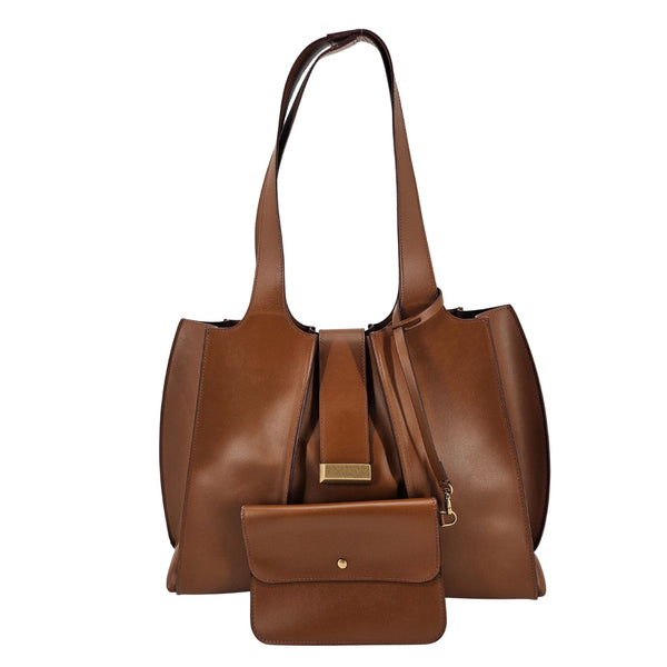 A mid-brown polished leather handbag with a wide opening, two top handles, a horizontal gold bar accent on the front, and a matching small brown pouch resting in front of it.