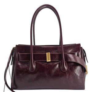 A sleek, burgundy polished leather handbag with two slender top handles and a horizontal gold bar accent on the front.