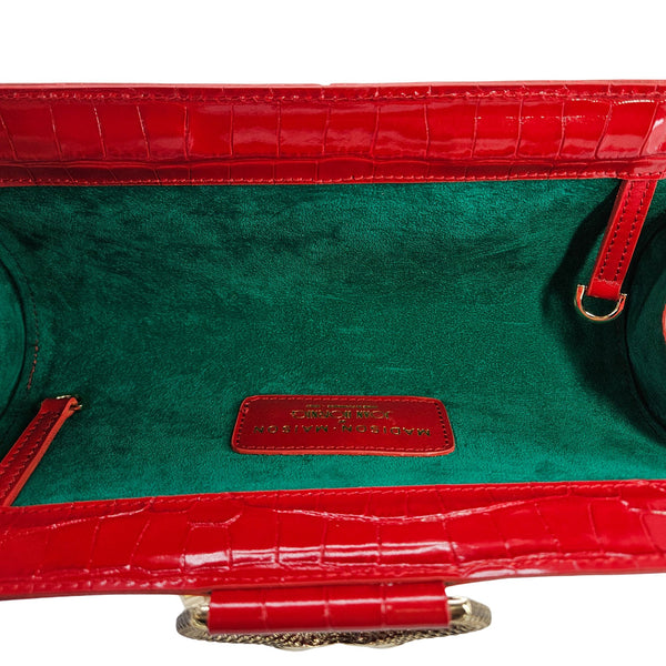 Red crocodile-patterned handbag with green interior and visible brand name.