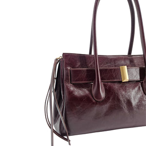 A sleek, burgundy polished leather handbag with two slender top handles and a horizontal gold bar accent on the front.