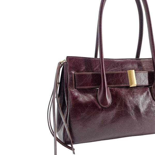 A sleek, burgundy polished leather handbag with two slender top handles and a horizontal gold bar accent on the front.
