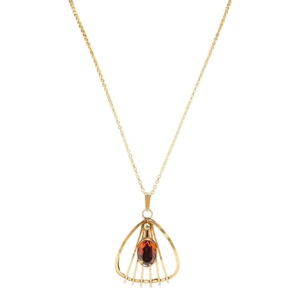 Gold necklace with a pendant featuring a red gemstone on a white background