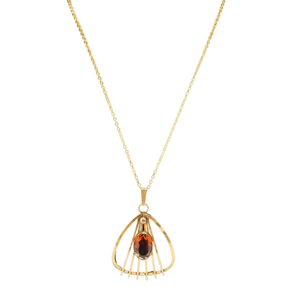 Gold necklace with a pendant featuring a red gemstone on a white background