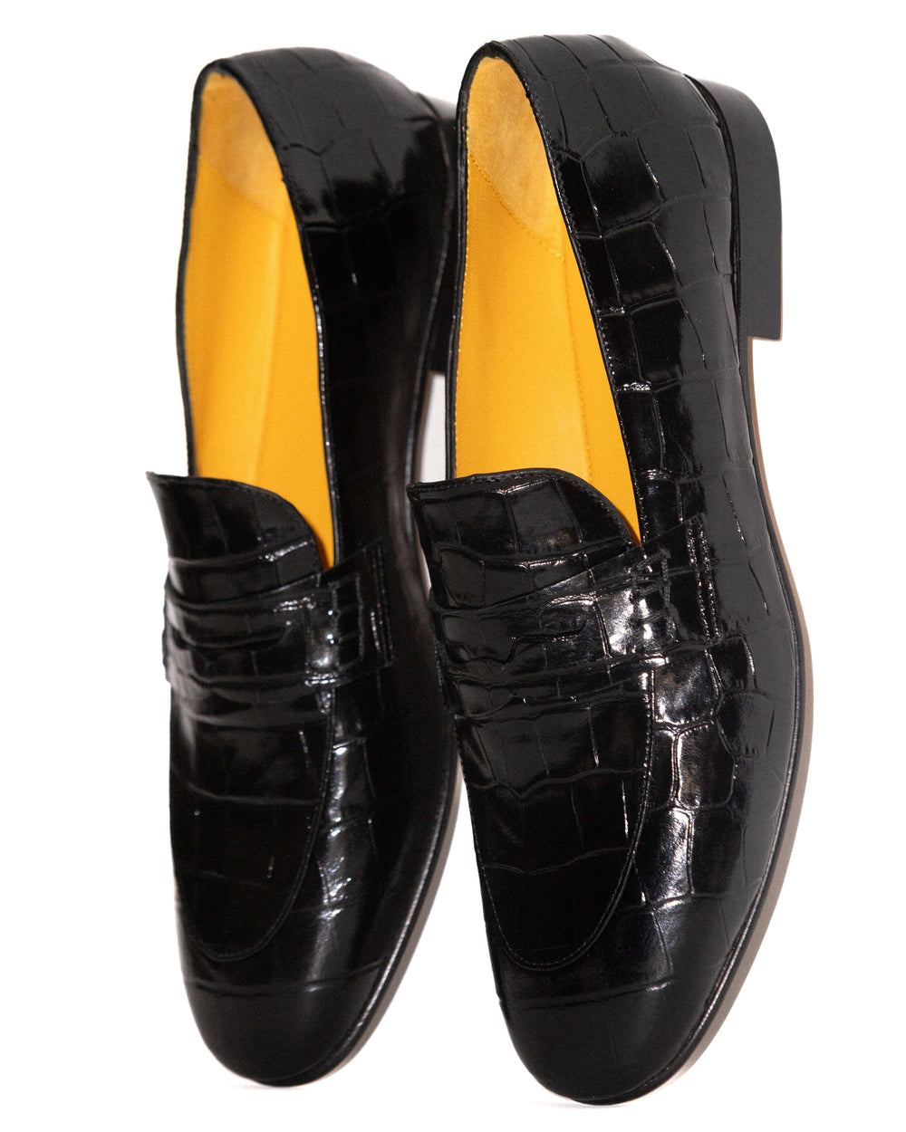 Black patent leather loafers with yellow lining on a white background