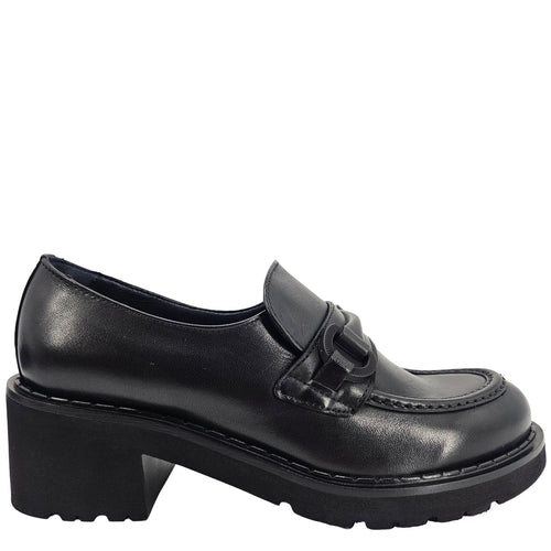 A close-up, eye-level shot of a single black leather lug sole loafer. The shoe features a chunky black lug sole with visible black stitching along the welt. A matching black rubber horse bit buckle adorns the vamp. The leather has a subtle pebbled texture. The background is solid white, emphasizing the shoe.
