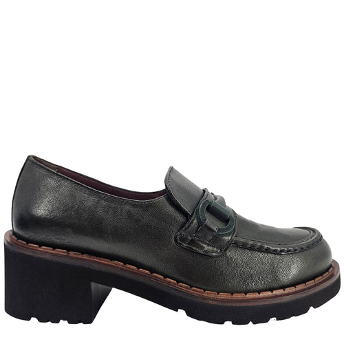 A close-up, eye-level shot of a single dark green leather lug sole loafer. The shoe features a chunky black lug sole with a visible brown welt stitching. A dark green rubber horse bit buckle adorns the vamp. The leather has a subtle pebbled texture. The background is solid white, emphasizing the shoe.