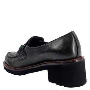 A close-up, eye-level shot of a single dark green leather lug sole loafer. The shoe features a chunky black lug sole with a visible brown welt stitching. A dark green rubber horse bit buckle adorns the vamp. The leather has a subtle pebbled texture. The background is solid white, emphasizing the shoe.