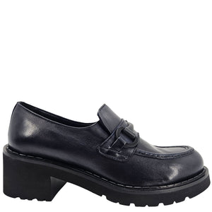 A close-up, eye-level shot of a single dark navy blue leather lug sole loafer. The shoe features a chunky black lug sole with visible dark stitching along the welt. A matching dark navy blue rubber horse bit buckle adorns the vamp. The leather has a subtle pebbled texture. The background is solid white, emphasizing the shoe.
