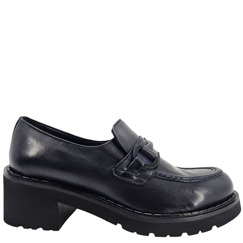 A close-up, eye-level shot of a single dark navy blue leather lug sole loafer. The shoe features a chunky black lug sole with visible dark stitching along the welt. A matching dark navy blue rubber horse bit buckle adorns the vamp. The leather has a subtle pebbled texture. The background is solid white, emphasizing the shoe.
