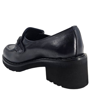 A close-up, eye-level shot of a single dark navy blue leather lug sole loafer. The shoe features a chunky black lug sole with visible dark stitching along the welt. A matching dark navy blue rubber horse bit buckle adorns the vamp. The leather has a subtle pebbled texture. The background is solid white, emphasizing the shoe.
