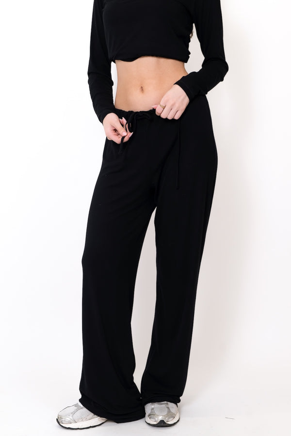 Person wearing black athletic pants and a black crop top on a white background