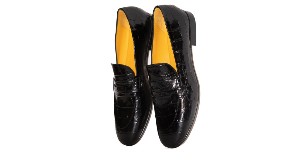 Black patent leather loafers with yellow lining on a white background