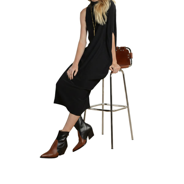 Woman in a black dress sitting on a stool with a brown handbag.