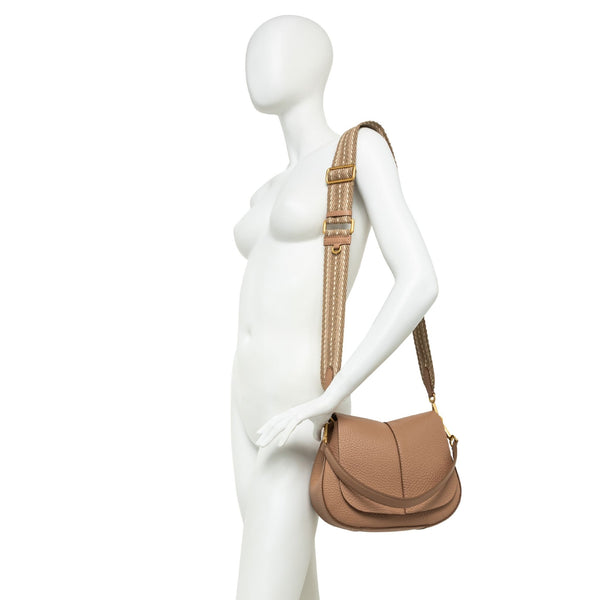 Mannequin wearing a tan leather handbag with a strap on a white background