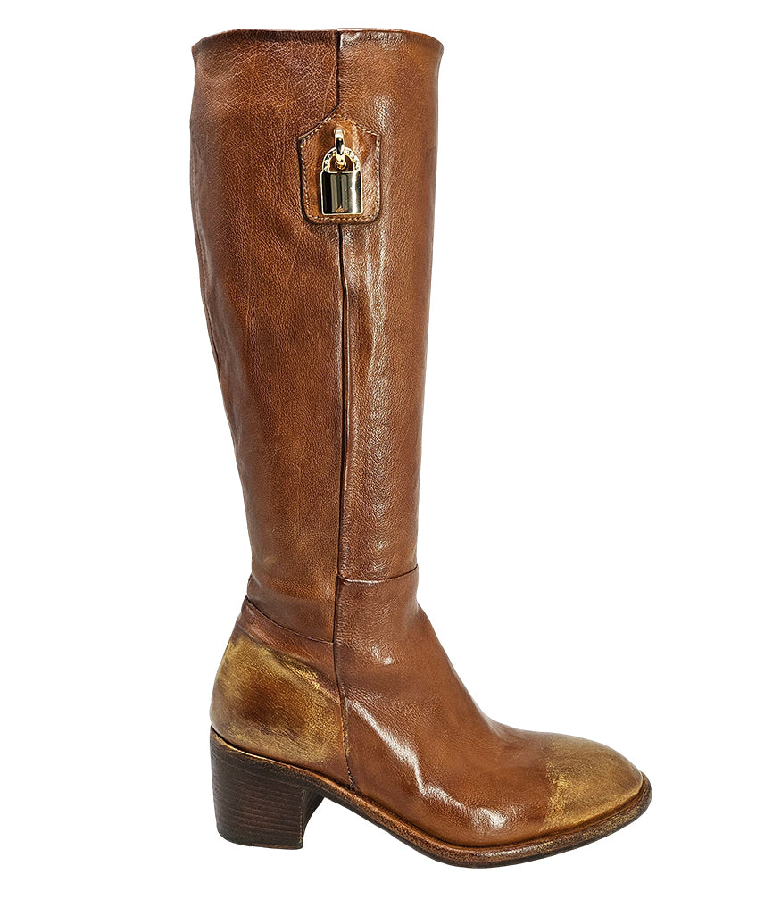 Tall leather boot featuring a softly rounded toe, mid-height stacked block heel, full side zipper for easy on and off, and a decorative metal lock accent near the top shaft. Crafted from premium leather with artisanal distressed detailing at the toe and h