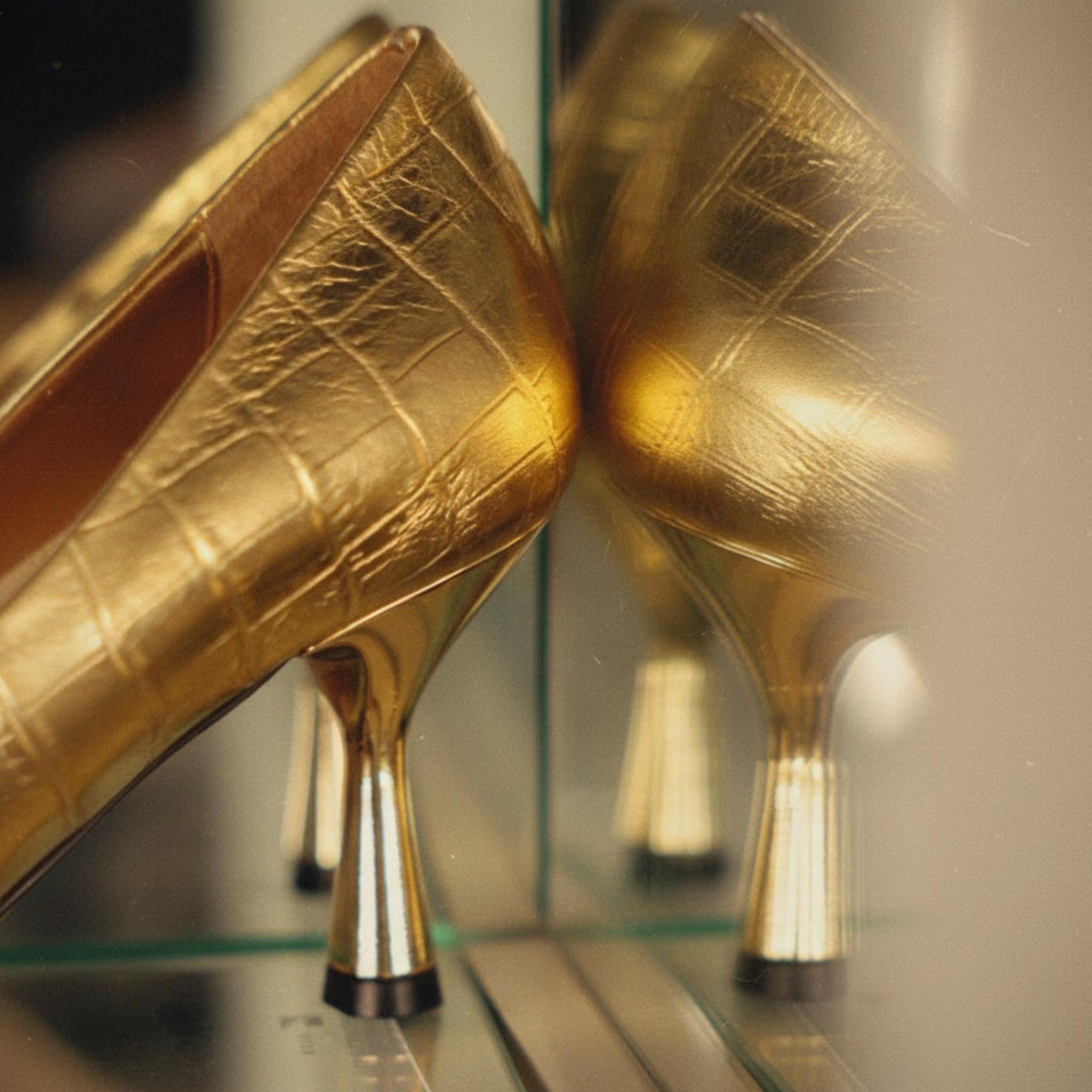 Pair of gold high-heeled shoes on a reflective surface