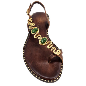 Brown sandal with gold and green embellishments on a white background
