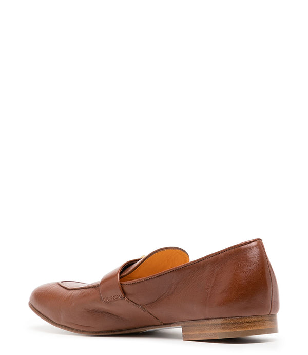 A leather loafer with a flat sole and rounded toe, featuring a small metal lock accent centered on the upper strap. Designed by Madison in Beverly Hills and handcrafted in Italy.