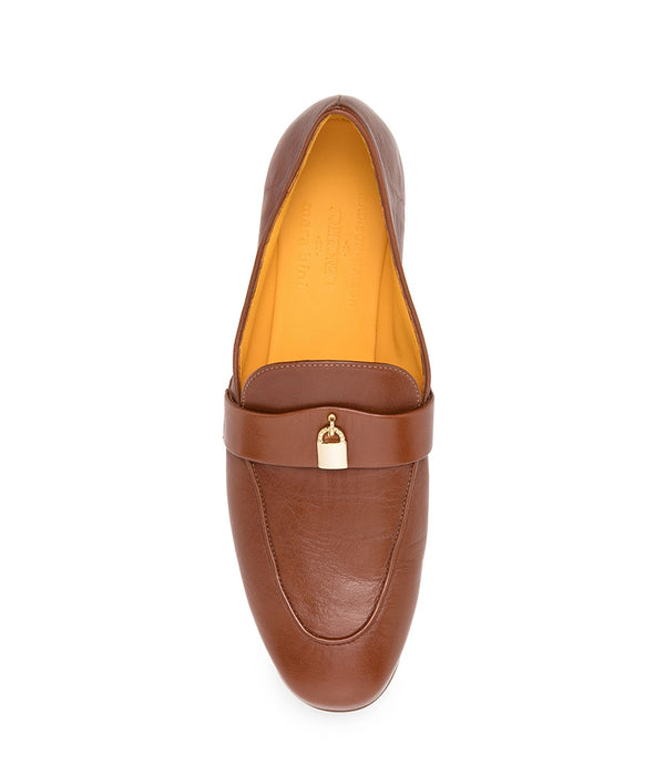 A leather loafer with a flat sole and rounded toe, featuring a small metal lock accent centered on the upper strap. Designed by Madison in Beverly Hills and handcrafted in Italy.