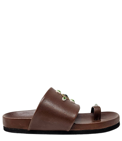 Open-toe flat sandal with a wide front strap and toe loop, embellished with central and side-set decorative stones. Features a contoured footbed and a low-profile sole.
