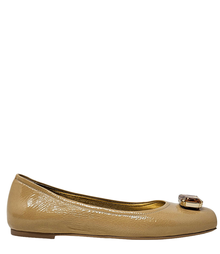 Four-angle view of a women's flat shoe with a glossy leather finish, rounded square toe, and a large faceted jewel embellishment at the toe. The shoe features a low-profile sole and a metallic-toned interior lining, displayed from side, angled, back, and