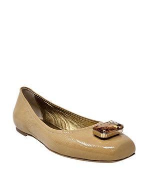 Four-angle view of a women's flat shoe with a glossy leather finish, rounded square toe, and a large faceted jewel embellishment at the toe. The shoe features a low-profile sole and a metallic-toned interior lining, displayed from side, angled, back, and
