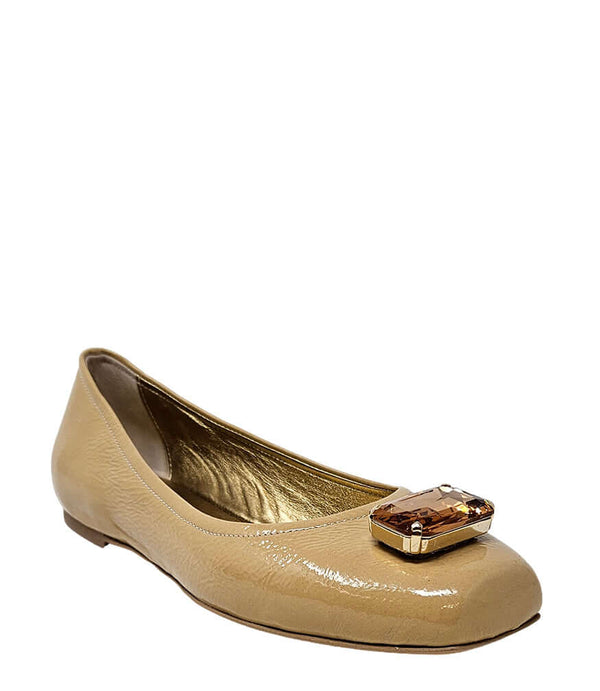 Four-angle view of a women's flat shoe with a glossy leather finish, rounded square toe, and a large faceted jewel embellishment at the toe. The shoe features a low-profile sole and a metallic-toned interior lining, displayed from side, angled, back, and
