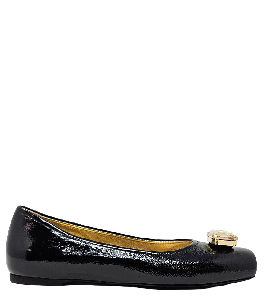 Four-angle view of a women's flat shoe with a glossy leather finish, rounded square toe, and a large faceted jewel embellishment at the toe. The shoe features a low-profile sole and a metallic-toned interior lining, displayed from side, angled, back, and
