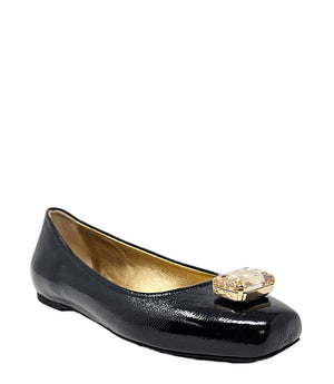 Four-angle view of a women's flat shoe with a glossy leather finish, rounded square toe, and a large faceted jewel embellishment at the toe. The shoe features a low-profile sole and a metallic-toned interior lining, displayed from side, angled, back, and