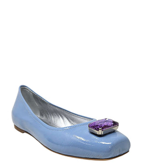 Four-angle view of a women's flat shoe with a glossy leather finish, rounded square toe, and a large faceted jewel embellishment at the toe. The shoe features a low-profile sole and a metallic-toned interior lining, displayed from side, angled, back, and